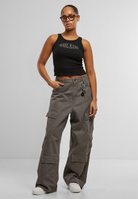 Top court noir à cannelures avec logo imprimé blanc, associé à un pantalon cargo gris ample doté de plusieurs poches et d'un clip pour porte-clés.
