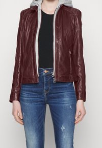 Giacca di pelle bordeaux con fodera del cappuccio grigia, design aderente, chiusura frontale con zip e dettagli di cuciture sottili; abbinata a jeans blu sfrangiati.