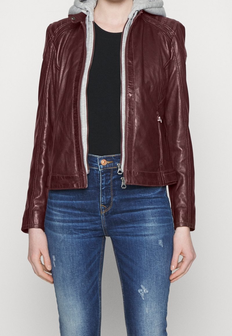 Giacca di pelle bordeaux con fodera del cappuccio grigia, design aderente, chiusura frontale con zip e dettagli di cuciture sottili; abbinata a jeans blu sfrangiati.