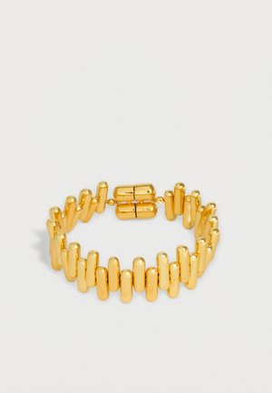 Bracciale tono oro con perline cilindriche verticali collegate in un anello continuo e chiusura magnetica su sfondo semplice.