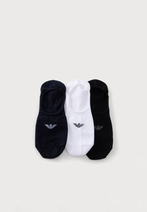 Trois chaussettes basses, bleu marine, blanches et noires, chacune ornée d’un petit logo, disposées sur un fond clair.