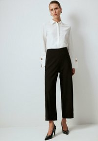 White long-sleeve shirt with a collared neck and gold button accents, paired with high-waisted black pants and black pointed-toe heels.