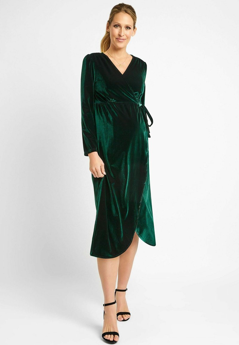 Grünes Samtwickelkleid mit langen Ärmeln, V-Ausschnitt, Gürtel in der Taille und knielangem Saum, das einen seitlichen Schlitz und eine weiche Textur aufweist.