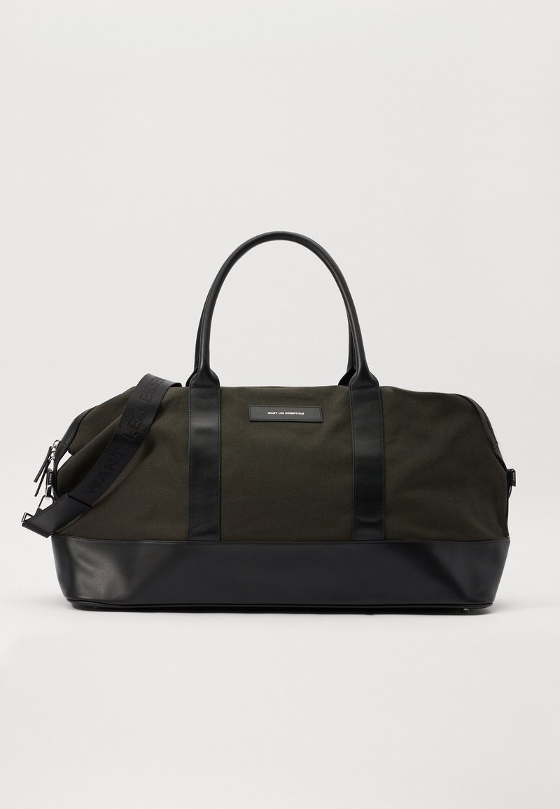 Green canvas duffel bag with black leather accents, rounded shape, dual handles, and adjustable shoulder strap featuring embossed text.