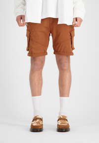 Shorts cargo marron avec des revers, dotés de poches latérales et arrière. Portés avec des chaussettes blanches et des chaussures marron à motifs.