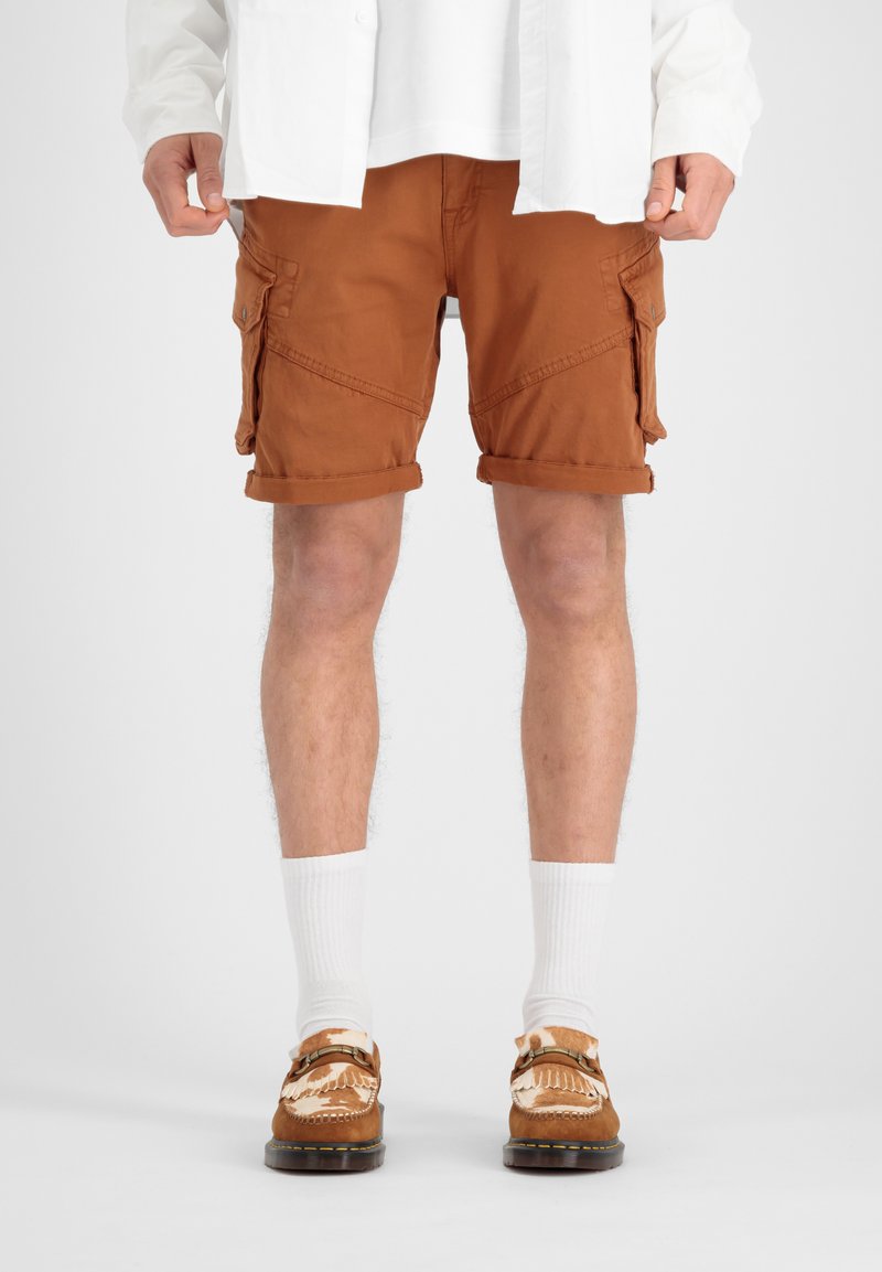 Shorts cargo marron avec des revers, dotés de poches latérales et arrière. Portés avec des chaussettes blanches et des chaussures marron à motifs.