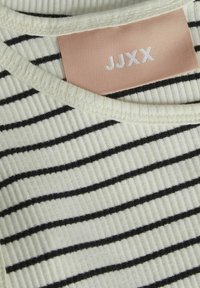 Top a maglia rigata in crema con strisce orizzontali nere. Collo rotondo e un etichetta con "JJXX" in bianco su uno sfondo rosa chiaro.