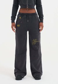 Svarta lösa sweatpants med dragsko i midjan, med gult och lila text och grafiska detaljer på benen och fickorna.