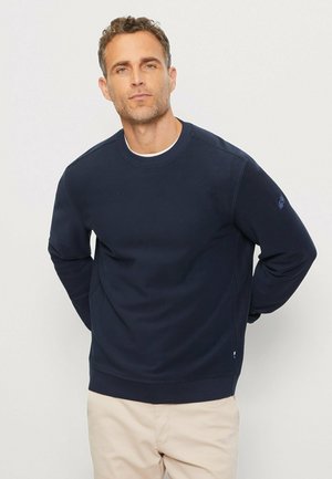 Navy blue sweatshirt made from soft fabric, featuring a crew neck and long sleeves. Includes subtle side seam detail and logo on sleeve.