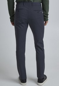 Marinblå skräddarsydda byxor med slät väv, slim fit och bakfickor med knappar. Att para ihop med svarta sneakers fulländar looken.