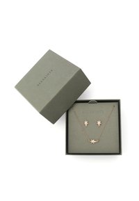 Ensemble collier et boucles d'oreilles en forme d'étoile en or rose, présenté dans une boîte ouverte de couleur vert foncé avec "ALLSAINTS" imprimé sur le couvercle et le plateau intérieur.