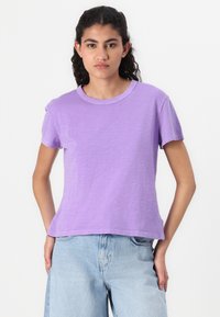 Lavendel kortermet t-skjorte i et mykt, lett stoff med rund hals og avslappet passform, sammen med lyseblå denimjeans.