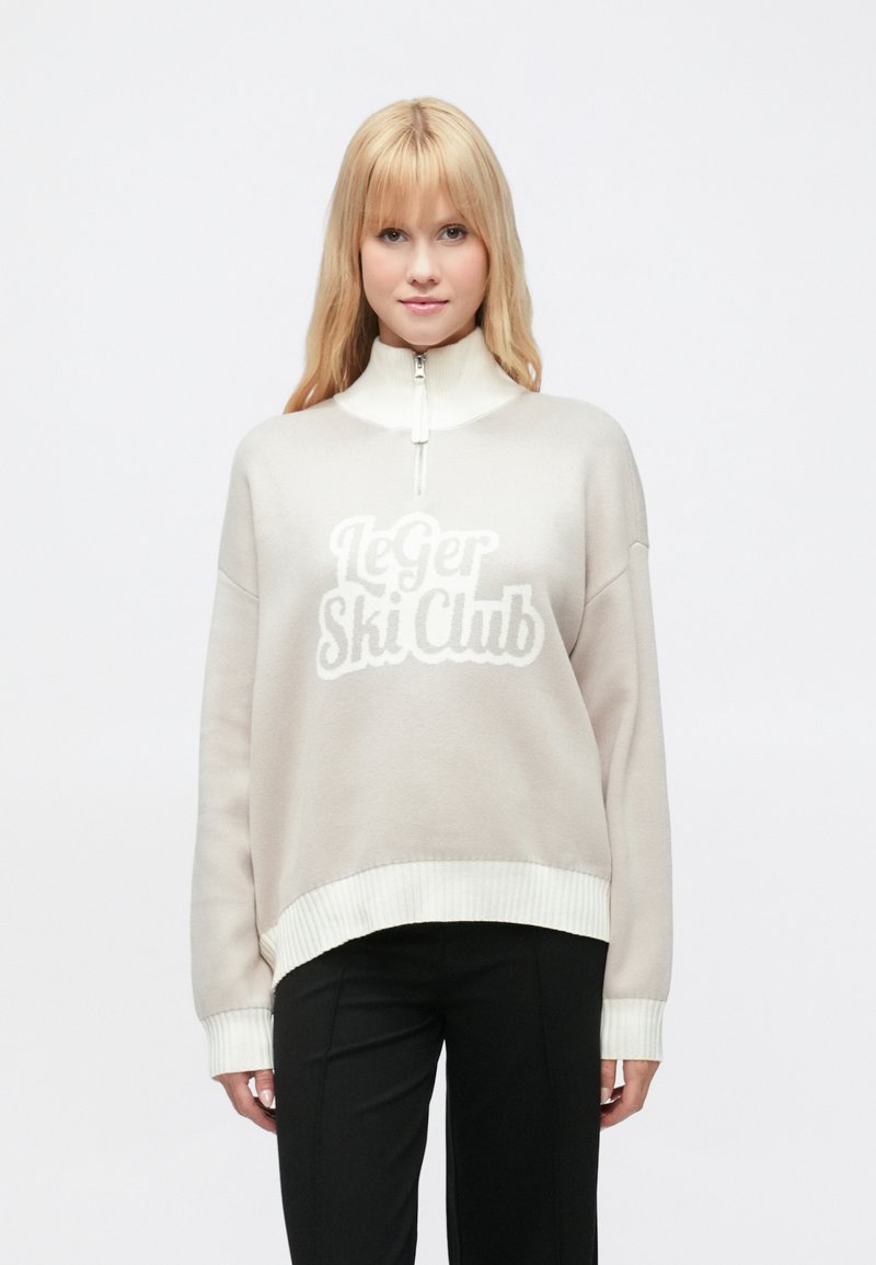 Világos bézs színű cipzáros pulóver fehér bordás mandzsettákkal és szegéllyel. Az elülső részen puha fehér betűkkel "Le Ger Ski Club" felirattal. Puha anyagból.