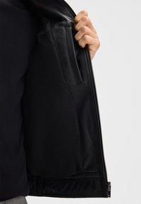 Giubbotto in pelle nera con apertura a zip; la fodera interna presenta una texture liscia e una tasca aggiuntiva sul lato sinistro.