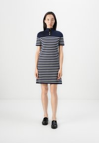 Marinblå og hvitmønstret polo-kjole med korte ermer, som har tre gullknapper ved kragen, over knelengde, kombinert med svarte loafers.