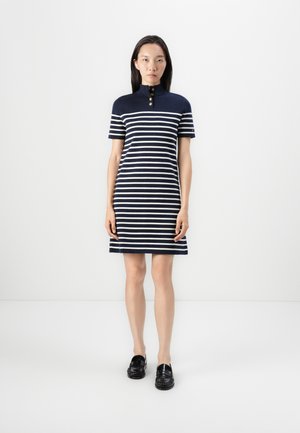 Navy and white striped polo dress with short sleeves, featuring three gold buttons at the collar, above knee length, paired with black loafers.