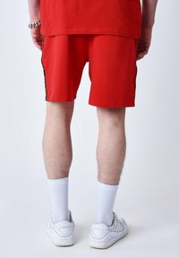 Pantalones cortos deportivos rojos con una textura suave y franjas laterales negras. Combinados con calcetines blancos hasta el tobillo y zapatillas blancas.