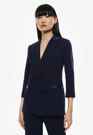 Blazer doppiopetto blu navy con revers in raso, maniche a tre quarti, chiusura con doppio bottone e tasche laterali. Tessuto dalla texture liscia.