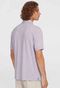 Polo à manches courtes en lavande clair, fabriqué en tissu texturé avec un col, des fentes latérales et une coupe décontractée.