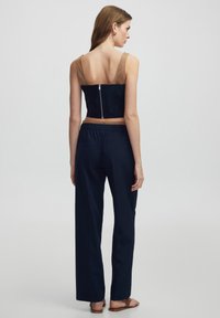 Haut court marine avec des bretelles beige et une fermeture éclair au dos, associé à un pantalon marine à coupe décontractée avec une taille élastique et des poches latérales.
