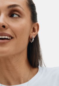 Hõbedast kõrvarõngad, millel on geomeetriline disain piikide ja tekstureeritud viimistlusega, kantud vasakul kõrvadel heleda tausta vastu.