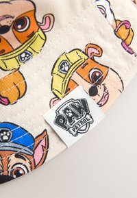 Mütze im Cap-Stil mit Cartoon-Hund-Illustrationen in Orange, Gelb und Blau, mit einem cremefarbenen Hintergrund und einem weißen Paw Patrol Logo-Anhänger.