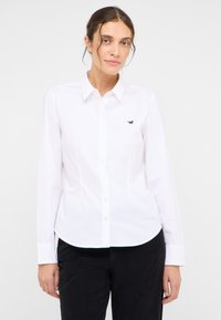 Biała koszula na guziki z długimi rękawami, zaostrzonym kołnierzykiem i zaokrąglonym dołem. Posiada małe logo ciemnoniebieskiego konia na lewej piersi.