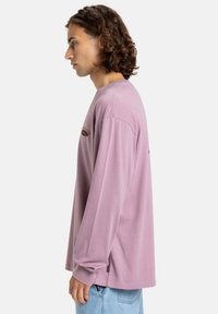 Langærmet, lyse lilla bomulds T-shirt med rund hals. Har et trykt logo på brystet og et label i sidesømmen.