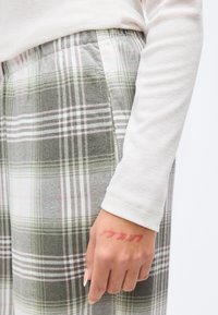 Πράσινο και λευκό καρό παντελόνι με ελαστική μέση, με λεπτές ροζ γραμμές. Ένα χέρι δείχνει ένα κόκκινο μελάνι στη παλάμη.