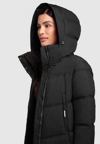 Schwarze Daunenjacke mit Kapuze, ausgestattet mit einem gesteppten Design und einem Frontreißverschluss. Akzentuiert mit Druckknöpfen und einem Logostick auf der Seite.