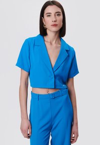 Blazer azul recortado con mangas cortas, solapa muesca, cierre de un solo botón, combinado con pantalones de tiro alto a juego. Tejido suave.