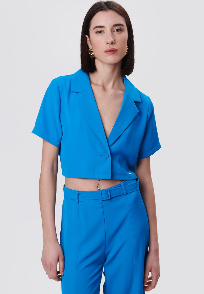 Blazer azul recortado con mangas cortas, solapa muesca, cierre de un solo botón, combinado con pantalones de tiro alto a juego. Tejido suave.