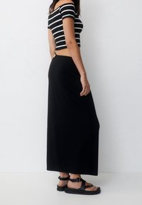 Una falda maxi negra combinada con un top recortado de rayas blancas y negras. El conjunto presenta una silueta ajustada y sandalias simples.
