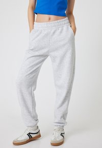 Lichtgrijze joggingsbroek met een geribde tailleband en boorden. Gemaakt van zacht materiaal, met zijzakken. Gedragen met witte sneakers.