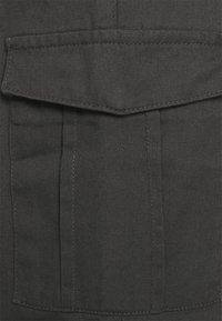 Tmavě šedá tkanina s viditelnou texturou. Obsahuje velkou kapsu se sklápěcí klapkou a kontrastním stehováním podél okrajů.