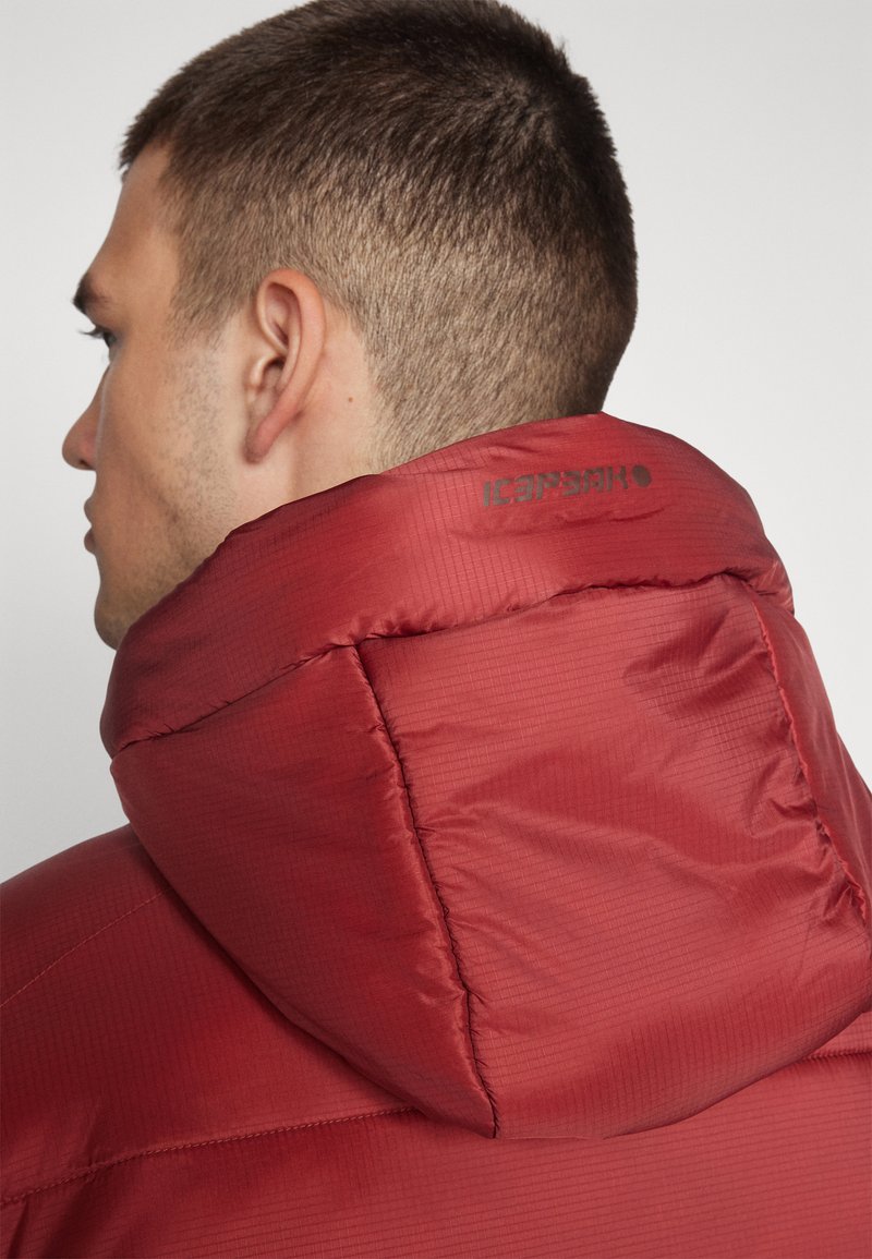 Rote Pufferjacke mit einer strukturierten Kapuze, aus einem strukturierten Stoff und mit einem Logo auf der Rückseite. Der Kragen hat eine genähte Verstärkung für zusätzlichen Halt.