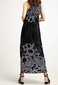 Svart maxikjol med vita paisley- och blommönster. Har en knytning vid bakhalsen och en flödande silhuett. Texturerad tyg med en jämn yta.