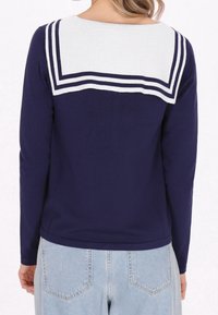 Námořnická halenka s dlouhým rukávem, zdobená bílým námořnickým límcem s kontrastními pruhy a žebrovanou texturou, spárovaná se světle modrými džíny.