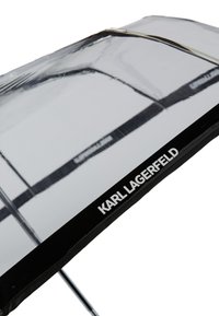 Przezroczysta parasolka z czarną krawędzią z logo "KARL LAGERFELD". Metalowa rama z przezroczystymi, błyszczącymi panelami oraz okrągłym uchwytem.