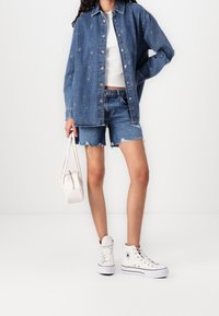 Denimová bunda s knoflíkovým zapínáním, modré barvy, mírně volnějšího střihu, doplněná o roztrhané džínové šortky a bílé vysoké tenisky.