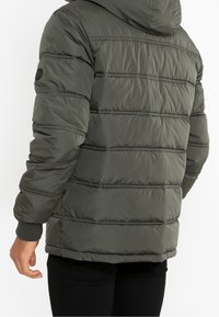 Kurtka puchowa w oliwkowym kolorze z poziomymi przeszyciami, kapturem i ściągaczami na rękawach. Posiada logo na lewym rękawie. Miękka, pikowana faktura.