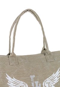 Bolsa de mano de lona en beige con un diseño de alas blanco impreso, que cuenta con dos asas largas y una costura superior reforzada para mayor durabilidad.