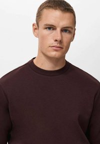 Bordo majica s crew vratom iz mekog materijala, s opuštenim krojem i suptilnim šavnim detaljima duž ramenskih šavova.