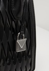 Sac à main noir avec une finition en cuir verni, présentant une texture tissée, du matériel en argent et un détail de cadenas triangulaire.