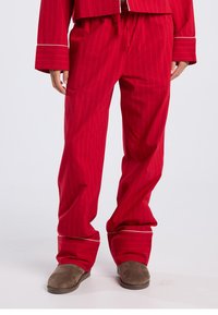 Punaraidallinen pyjamapuku, joka sisältää rentolaatuisen takin ja housut, joissa on valkoiset korostukset ja pehmeä, teksturoitu kangas. Ruskeat tohvelit.