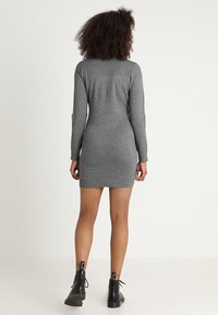 Vestido gris de manga larga ajustado al cuerpo, de largo hasta el muslo, hecho de tejido de punto texturizado, combinado con botines negros de cordones hasta el tobillo.