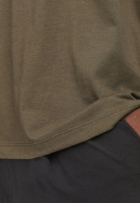 Olive green cotton t-shirt with a smooth texture, featuring a straight hem and short sleeves, positioned above a pair of black pants.