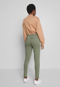 Hellbraun sweatshirt kombiniert mit grünen Jogginghosen. Die Hosen haben eine schmal zulaufende Passform und einen elastischen Bund; beide sind aus weichem, bequemem Stoff gefertigt.