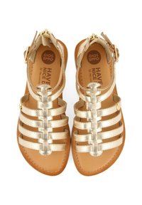 Sandalias doradas con tiras, de suela plana, con tiras de cuero y cierre de hebilla, superficie lisa y plantilla marrón con logo.