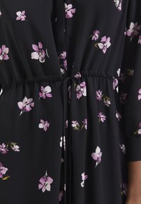 Vestido negro de flores con tejido ligero, cintura elástica y cierre con cordón, adornado con pequeños patrones de flores en rosa y blanco.